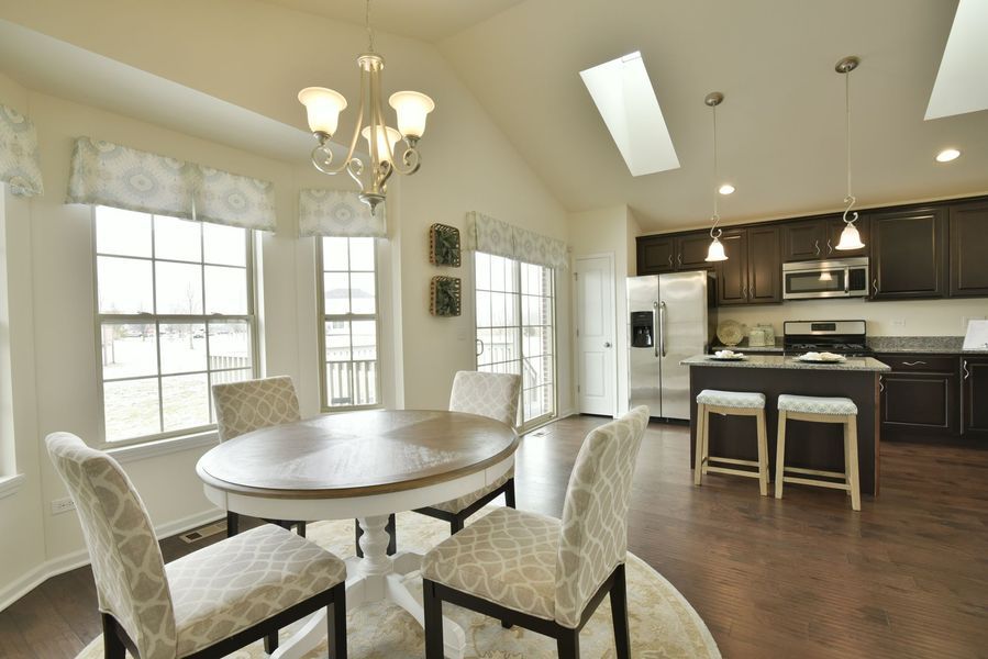 Dining area with oval table, chairs, chandelier, and kitchen with dark cabinets, stainless appliances, and skylight.