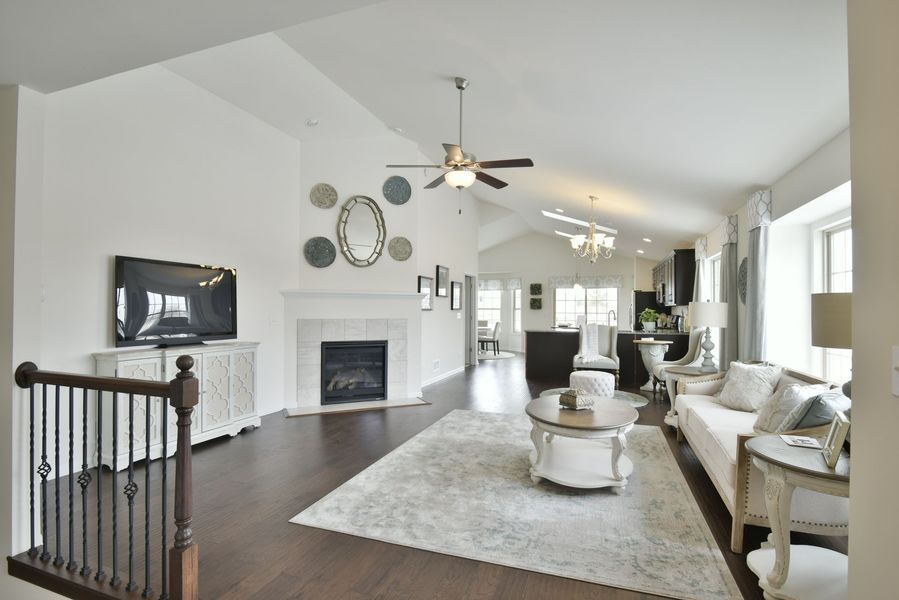 Spacious living room with vaulted ceiling, fireplace, white furniture, and dark wood floors.