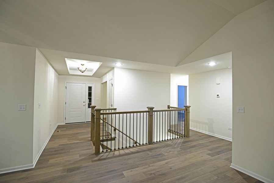 Interior view of a hallway with a wooden staircase and door. Light-colored walls and flooring.
