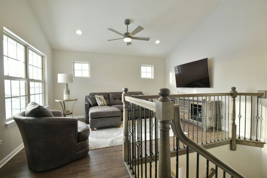 Living room with gray furniture, TV, and staircase, in a house with natural light.