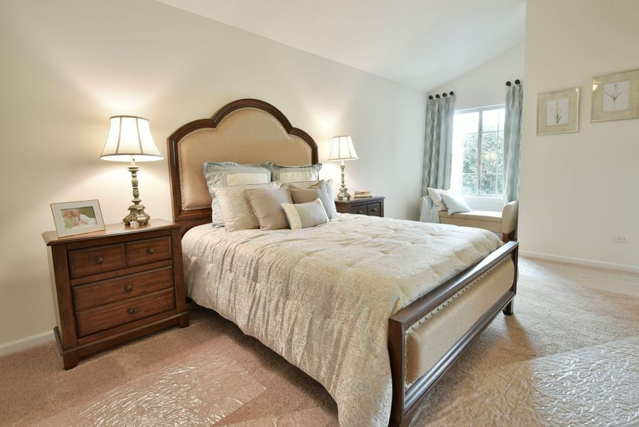 Bedroom with bed, nightstands, lamps, and a window. Beige and brown tones throughout.