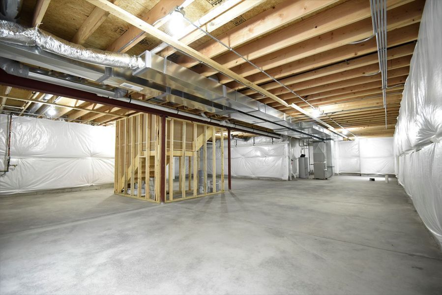 Unfinished basement with exposed wooden beams, concrete floor, and insulation on the walls.