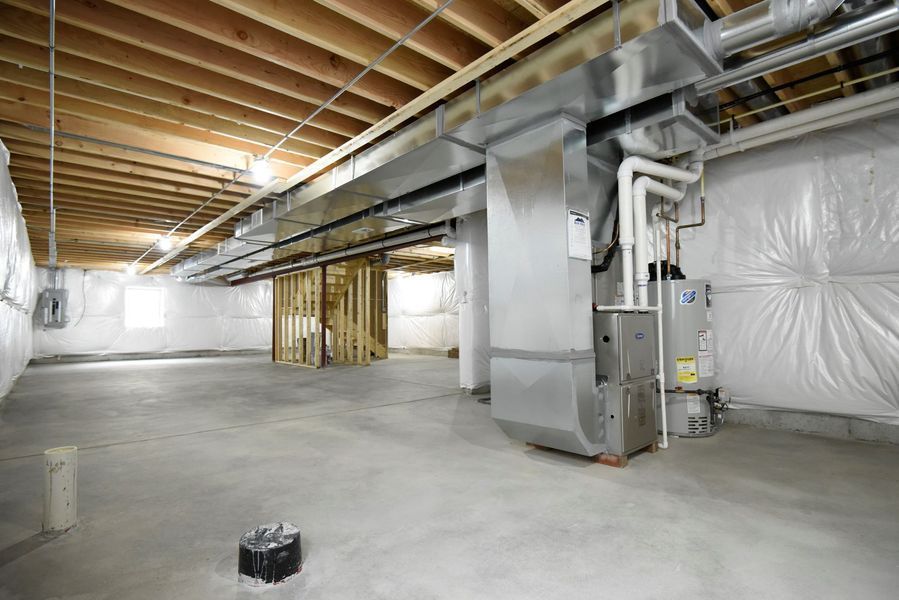 Unfinished basement with HVAC system, concrete floor, wooden beams, and white plastic wall covering.