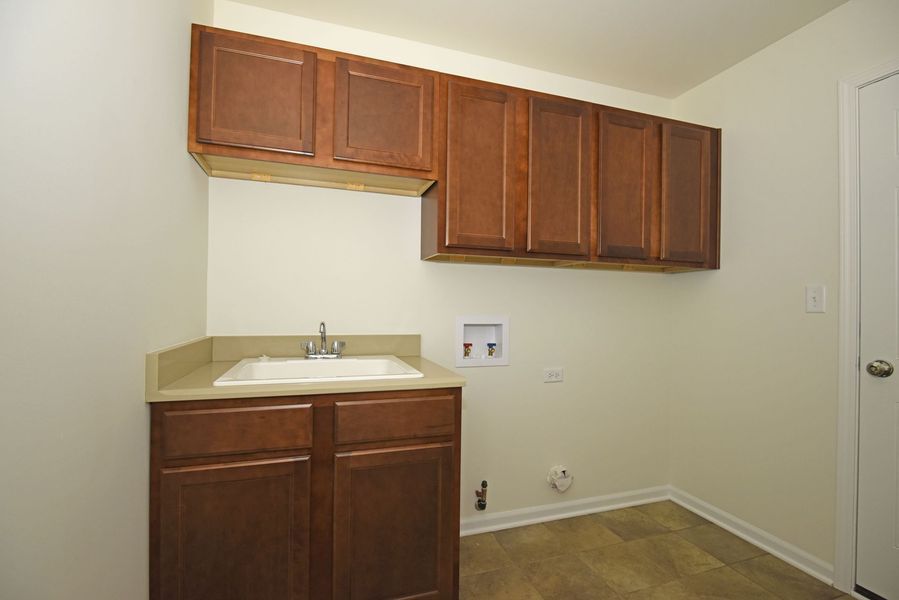 Laundry room with dark brown cabinets, a white sink, and white walls.