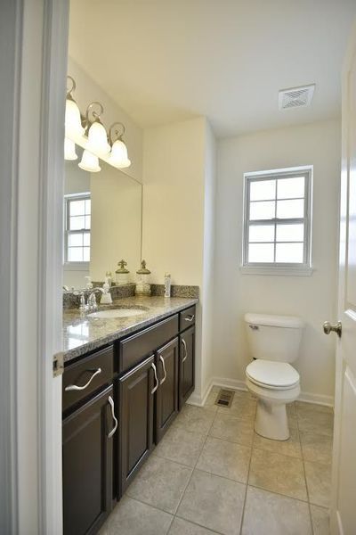 Bathroom with dark brown vanity, white toilet, and small window.