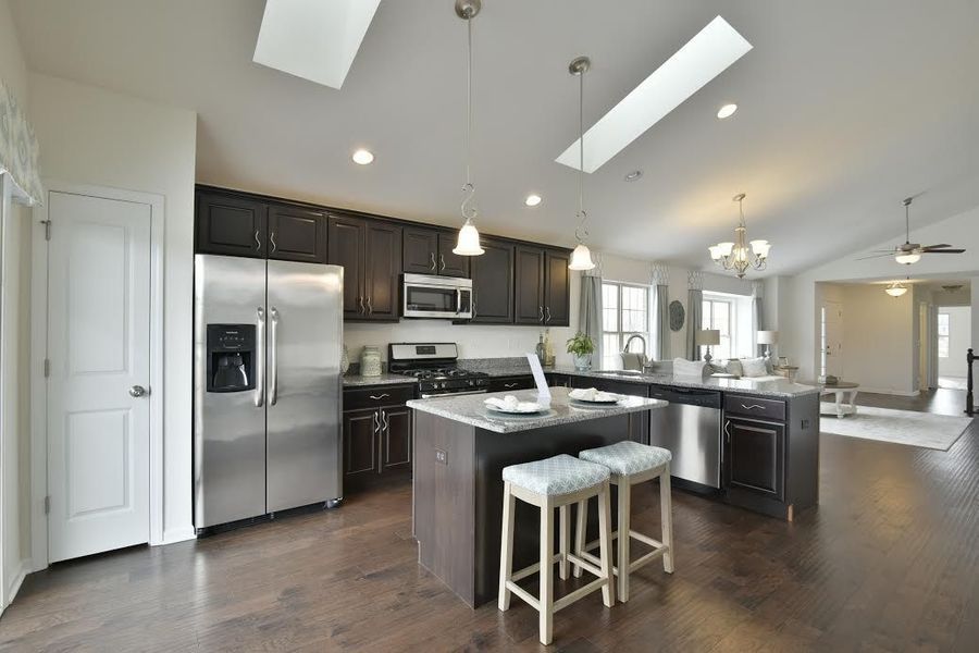 Kitchen with dark brown cabinets, stainless steel appliances, and island with two stools.