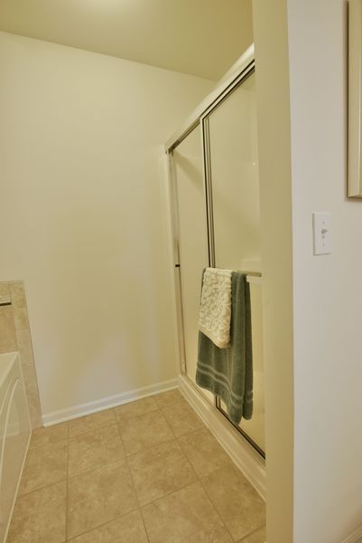 Bathroom with glass shower door, beige tiled floor, and two towels hanging inside.