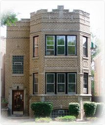 Beige brick two-story building with multiple windows, arched doorway, and small bushes.