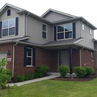 Two-story house with gray siding, dark shutters, brick facade, and green lawn.