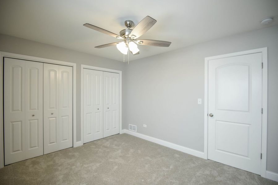 Empty bedroom with two closets, a door, a ceiling fan, and carpet.