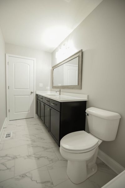 Bathroom with a dark vanity, white toilet, marble floors, and a door.