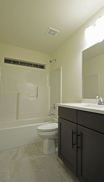 Bathroom with white tub, toilet, and vanity with dark cabinets.