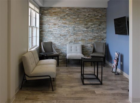Waiting room with stone accent wall, chairs, a small table, and a window.