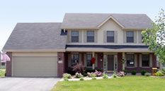 Two-story suburban house with a gray roof and brick facade. A garage door is on the left.