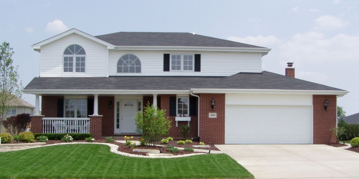 Two-story white house with brick accents, black shutters, and a green lawn.