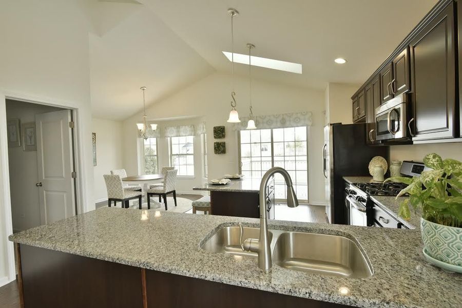 Kitchen with granite countertop, stainless steel sink, dark cabinets, and dining area in the background.