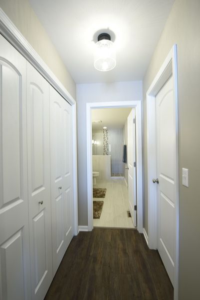 Narrow hallway with white doors, closet on left, and open bathroom door ahead.