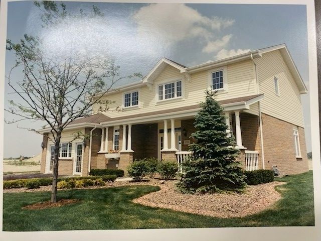 House with cream siding, brick base, porch, and landscaped yard.