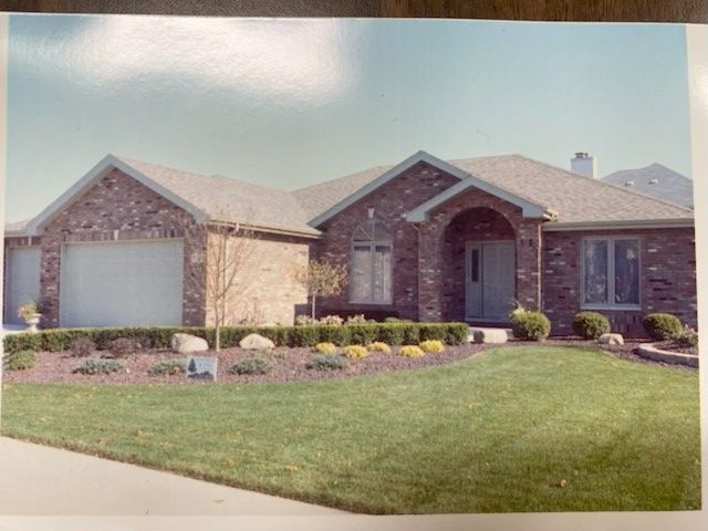 Brick house with attached garage, landscaped lawn, arched doorway, and windows.