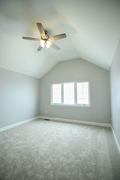 Empty room with vaulted ceiling, neutral paint, carpet, ceiling fan, and window.