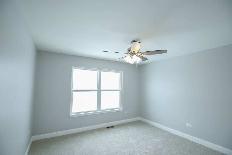 Empty bedroom with gray walls, window, ceiling fan, and carpet.