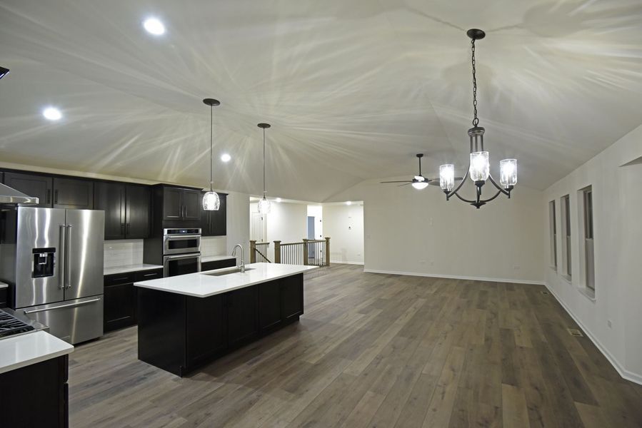 Modern kitchen and living area with dark cabinets, white countertops, and wood flooring.