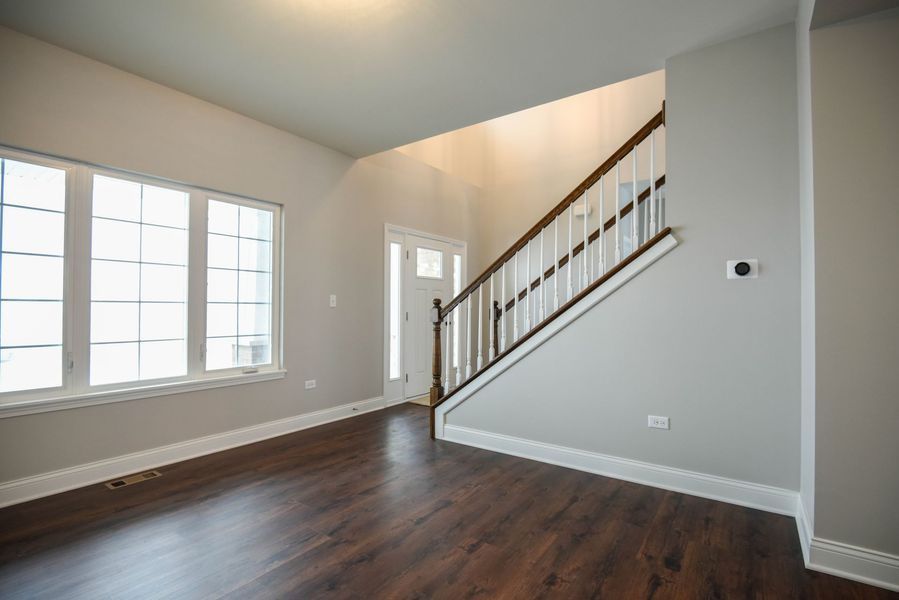 Empty living room with dark wood floor, stairs with white and brown railing, and a window.