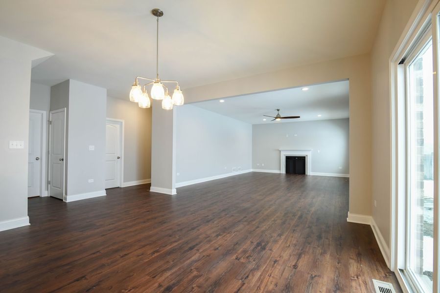 Empty, open-concept living space with dark wood floors, light walls, and a chandelier.
