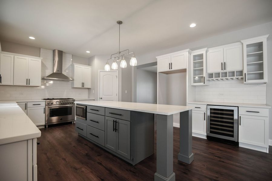 Modern kitchen with gray island, white cabinets, stainless steel appliances, and dark wood floors.