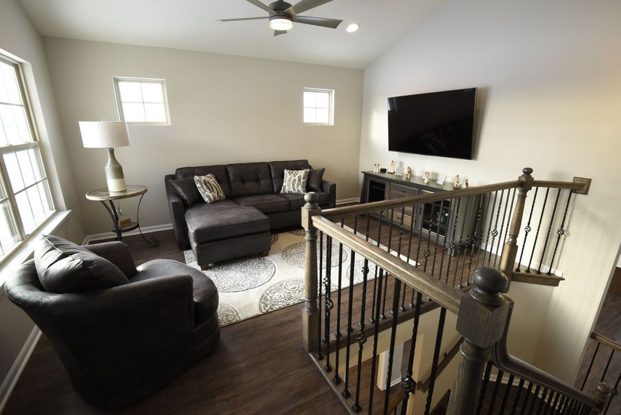 Living room with dark gray furniture, hardwood floors, and a stairway.