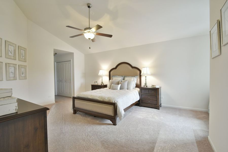 Bedroom with bed, nightstands, and artwork on cream-colored walls, with a vaulted ceiling and carpeted floor.