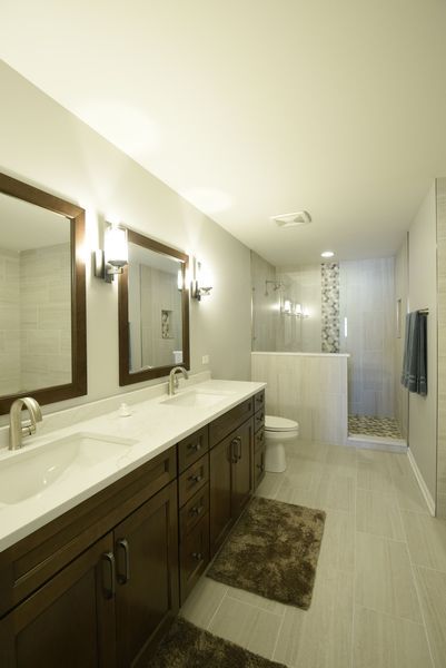 Bathroom with double sinks, dark wood vanity, gray tile, and a glass shower.