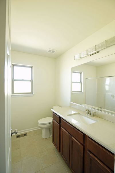 Bathroom with a toilet, vanity with sink, mirror, and a window. Beige walls and brown cabinets.