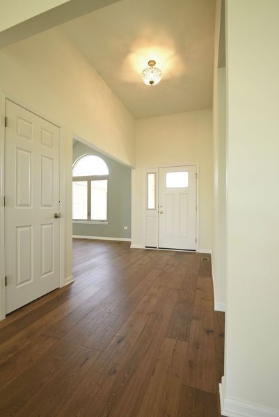 Entryway with wood floor, white doors, and arched window in the background.