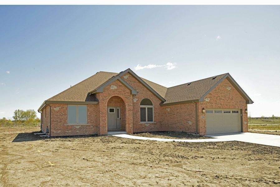Brick ranch-style house on a bare lot under a blue sky, with a driveway and attached garage.