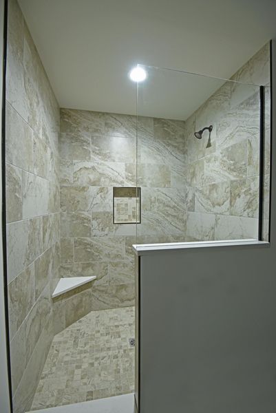 Shower stall with beige tile walls, glass door, and built-in bench.