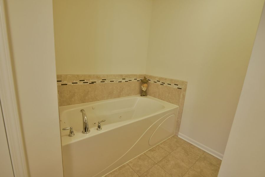 Bathtub alcove with white tub, beige tile surround, and light beige walls.