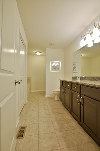 Bathroom with brown cabinets, large mirror, and tan tiled floor.