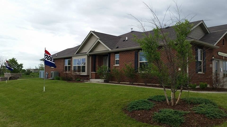 Red brick house with manicured lawn, shrubs, and a flag. Cloudy sky.