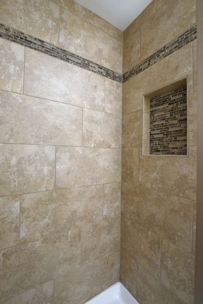 Shower stall with beige tiles and a dark accent stripe; built-in niche.