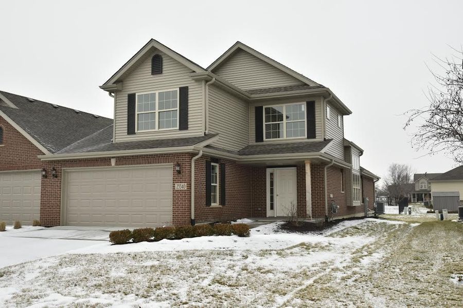 Two-story house with brick and siding, a two-car garage, and snow-covered yard on an overcast day.