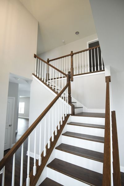Wooden staircase with white spindles, leading up to a second floor landing.