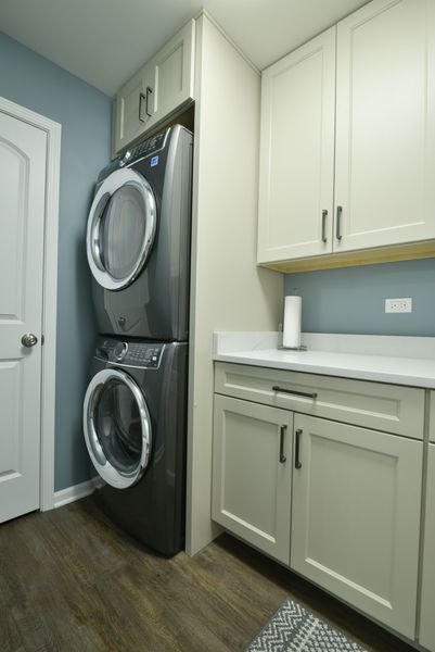 Laundry room with stacked washer/dryer, light cabinets, and blue wall.