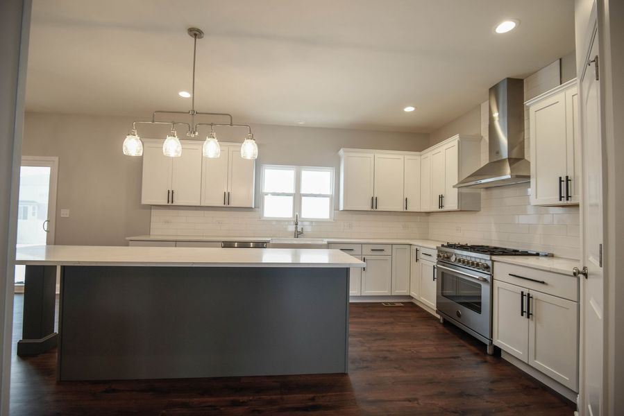 Modern kitchen with white cabinets, gray island, stainless steel appliances, and dark wood floors.