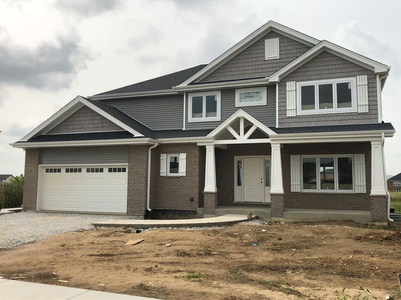 Two-story house under construction with gray siding, brick facade, white trim, and a white garage door.