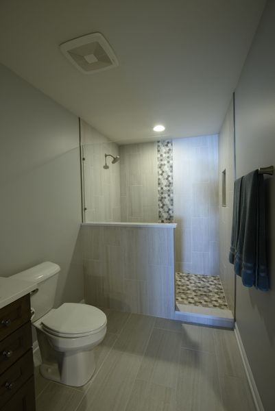 Bathroom with walk-in shower, toilet, and towel rack. Light gray and white tiled walls and floor.