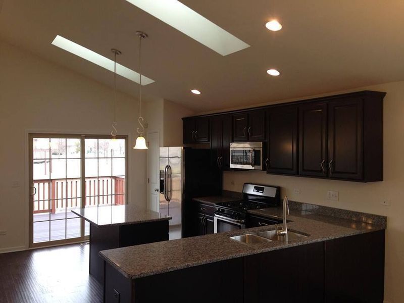 Kitchen with dark cabinets, granite countertops, island, and skylights; sliding door to deck.