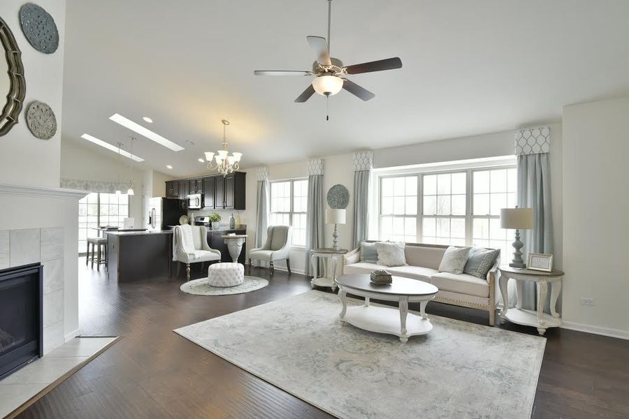 Spacious living room with fireplace, dark wood floors, and neutral furnishings; includes a ceiling fan, and large windows.