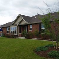 Brick ranch-style house with green lawn and landscaping under a cloudy sky.