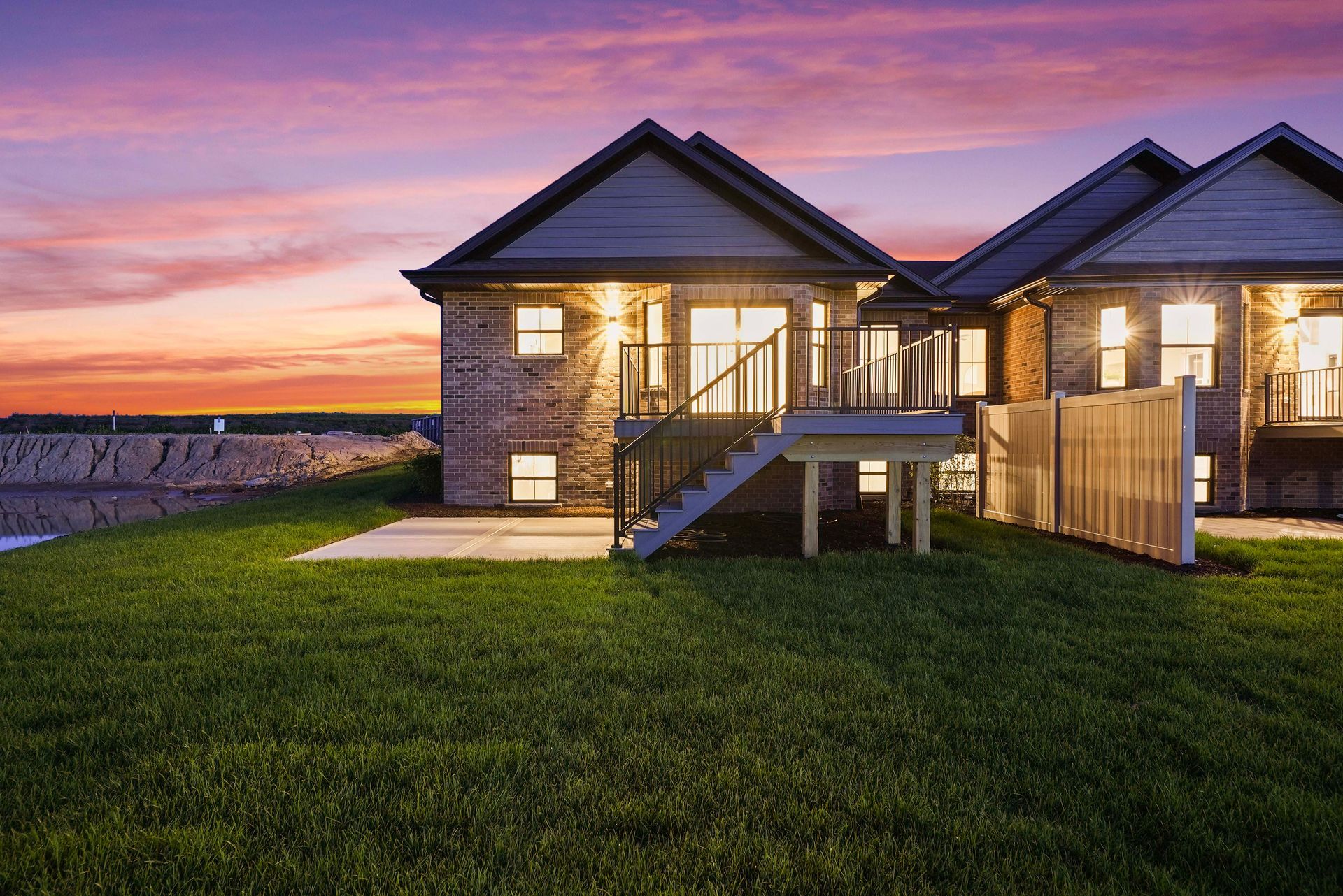 Suburban house with lit windows at dusk, green lawn, and a pink-purple sunset sky